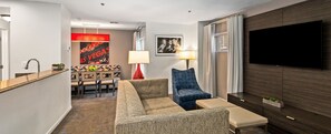 Un salon moderne comprenant un canapé, un fauteuil bleu, un téléviseur et un coin repas avec une table et des chaises.