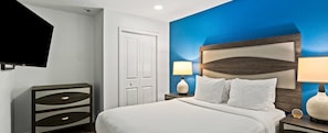 Une chambre d’hôtel avec un lit, des tables de chevet, un téléviseur et un mur agrémenté d’une touche de couleur bleue.