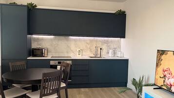 Een moderne keuken met donkere kasten, een eettafel met stoelen, een kroonluchter en een flatscreen televisie op een standaard.