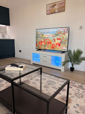 A modern living room with a flat-screen TV, a glass coffee table, and a patterned rug. - 4-Bedrooms Flat Walk To Wembley Stadium (Wembley)