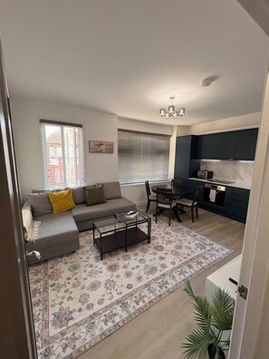 A living room with a sofa, coffee table, and a dining area with chairs and a table. - 4-Bedrooms Flat Walk To Wembley Stadium (Wembley)
