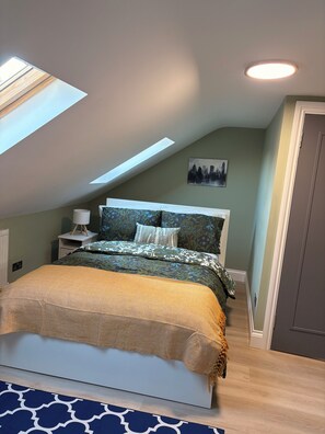 A bedroom with a skylight, a bed with patterned bedding, a nightstand with a lamp, and a cityscape painting on the wall. - 4-Bedrooms Flat Walk To Wembley Stadium (Wembley)