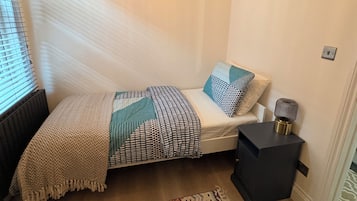 A small, well-lit bedroom with a bed, bedside lamp, and a patterned rug.