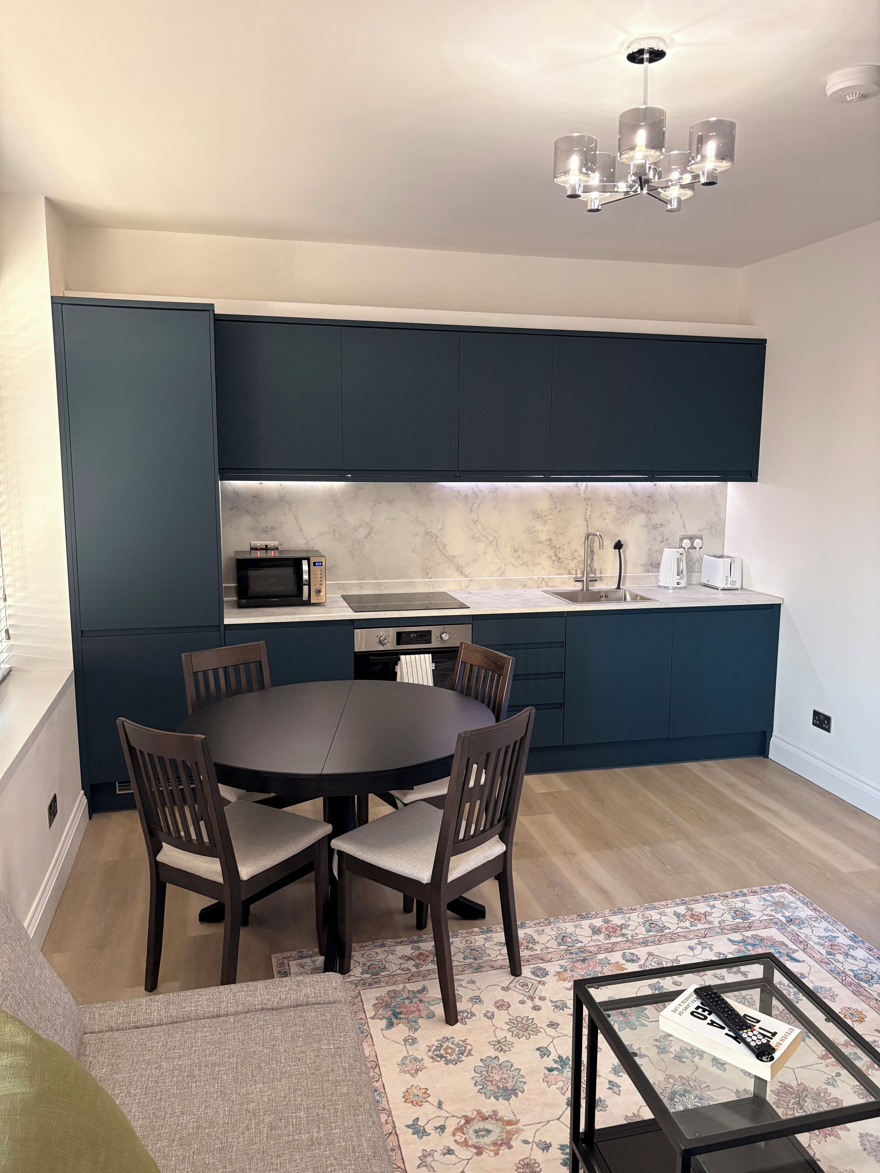 A modern kitchen with dark cabinetry, a round dining table, and a chandelier.