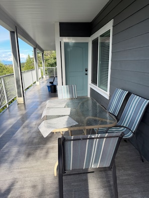 A covered outdoor patio with a glass-top table and striped chairs, a door, and a view of the surrounding area. - Ocean View Haven, Ocean Views • Stunning Sunsets • Fully Equipped Home •  (Nanaimo)