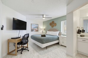 Ein Schlafzimmer mit Bett, Schreibtisch, Stuhl, Fernseher und Deckenventilator.