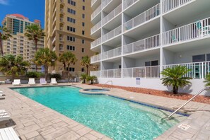 A swimming pool with lounge chairs and palm trees, surrounded by a building with balconies. - Four Winds 801 - Beachfront Corner - Pool & Hot Tub (Orange Beach)