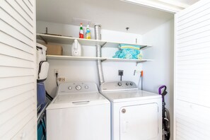 A laundry room with two stacked washers and dryers, a shelf with cleaning supplies, and a vacuum cleaner. - Four Winds 801 - Beachfront Corner - Pool & Hot Tub (Orange Beach)