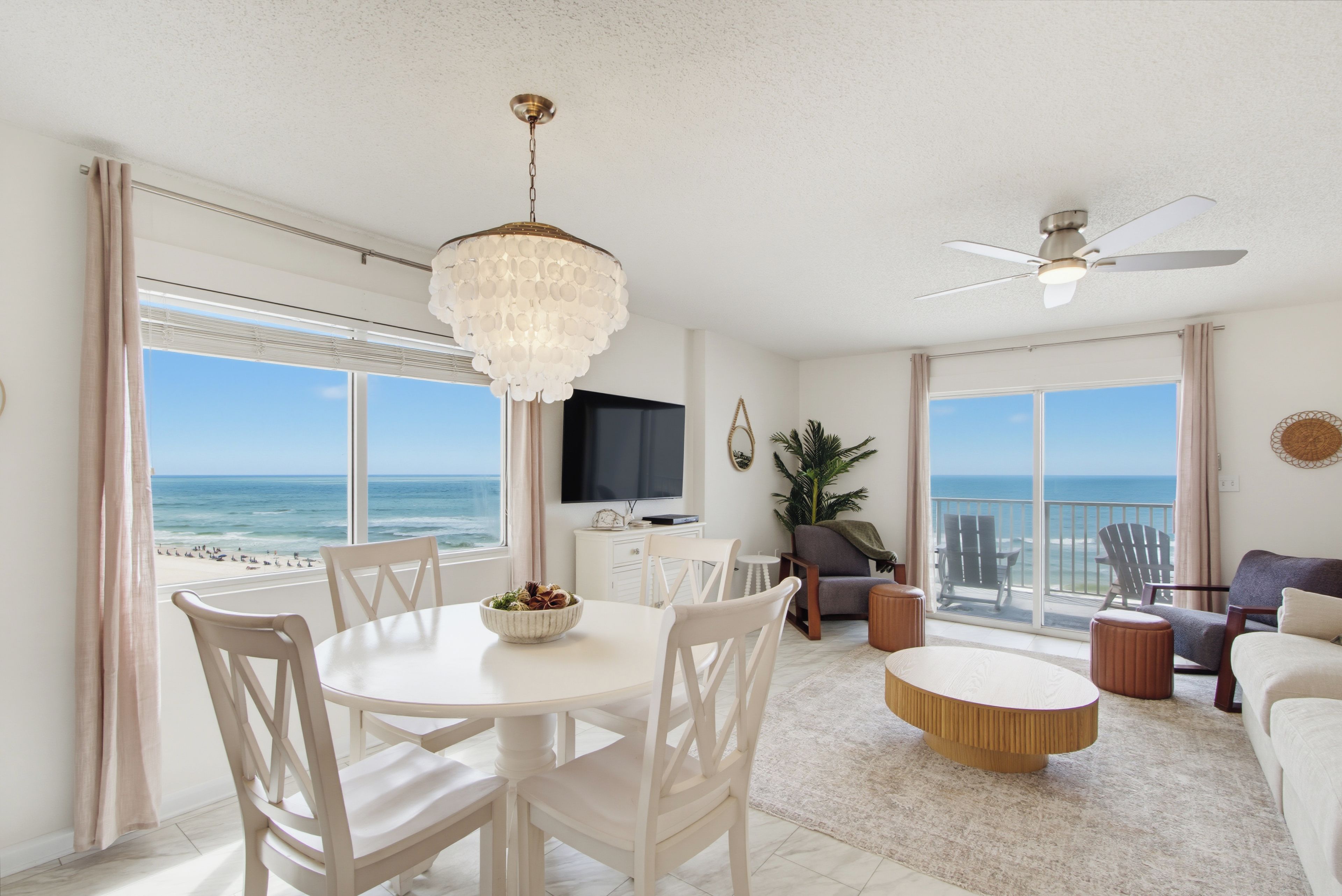 A spacious living area with a dining table, chairs, a ceiling fan, and a view of the ocean.