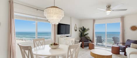 A spacious living area with a dining table, chairs, a ceiling fan, and a view of the ocean.