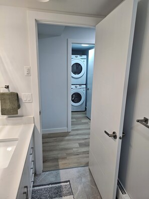 Une buanderie avec deux machines à laver superposées, une porte blanche et un plancher en bois.