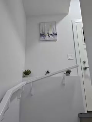 Un escalier avec une rampe blanche, une petite plante en pot sur la plateforme, et un tableau représentant des voiliers accroché au mur.