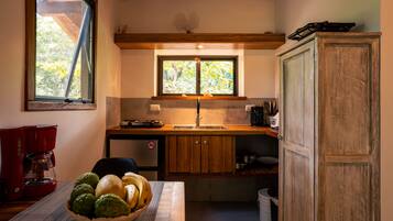 Une cuisine compacte dotée d’un plan de travail en bois, d’une cuisinière, d’un évier et d’une fenêtre donnant sur un paysage verdoyant.