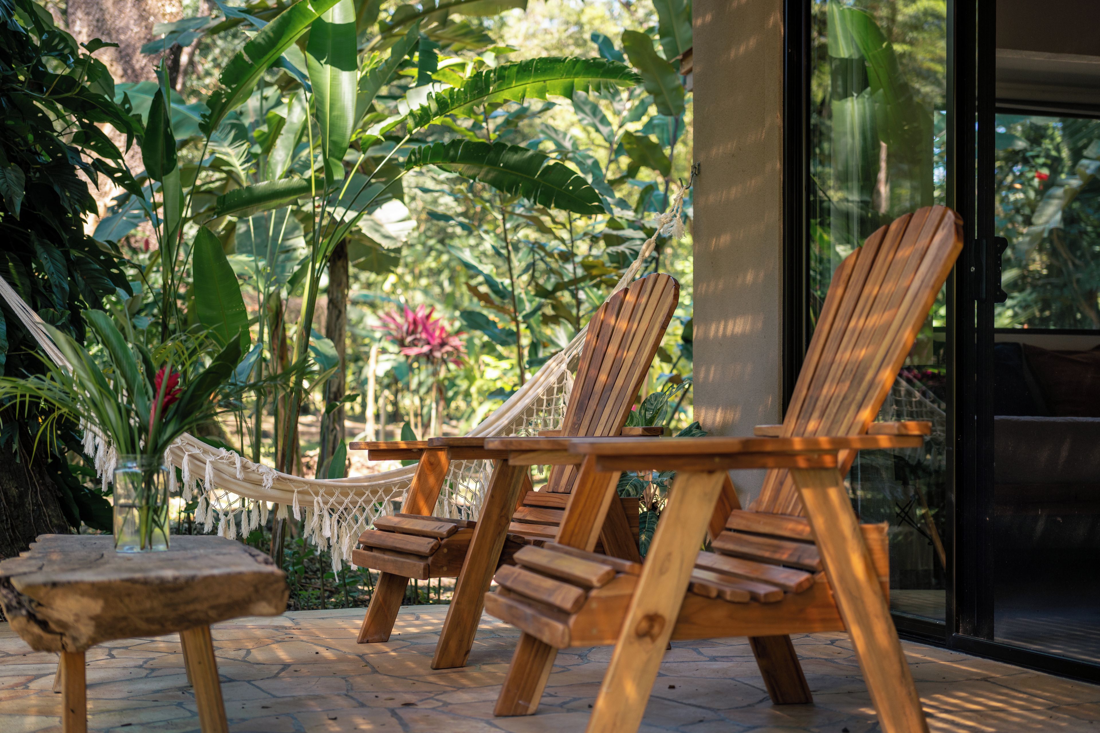 A hammock chair set up on a stone patio with a view of lush tropical plants.