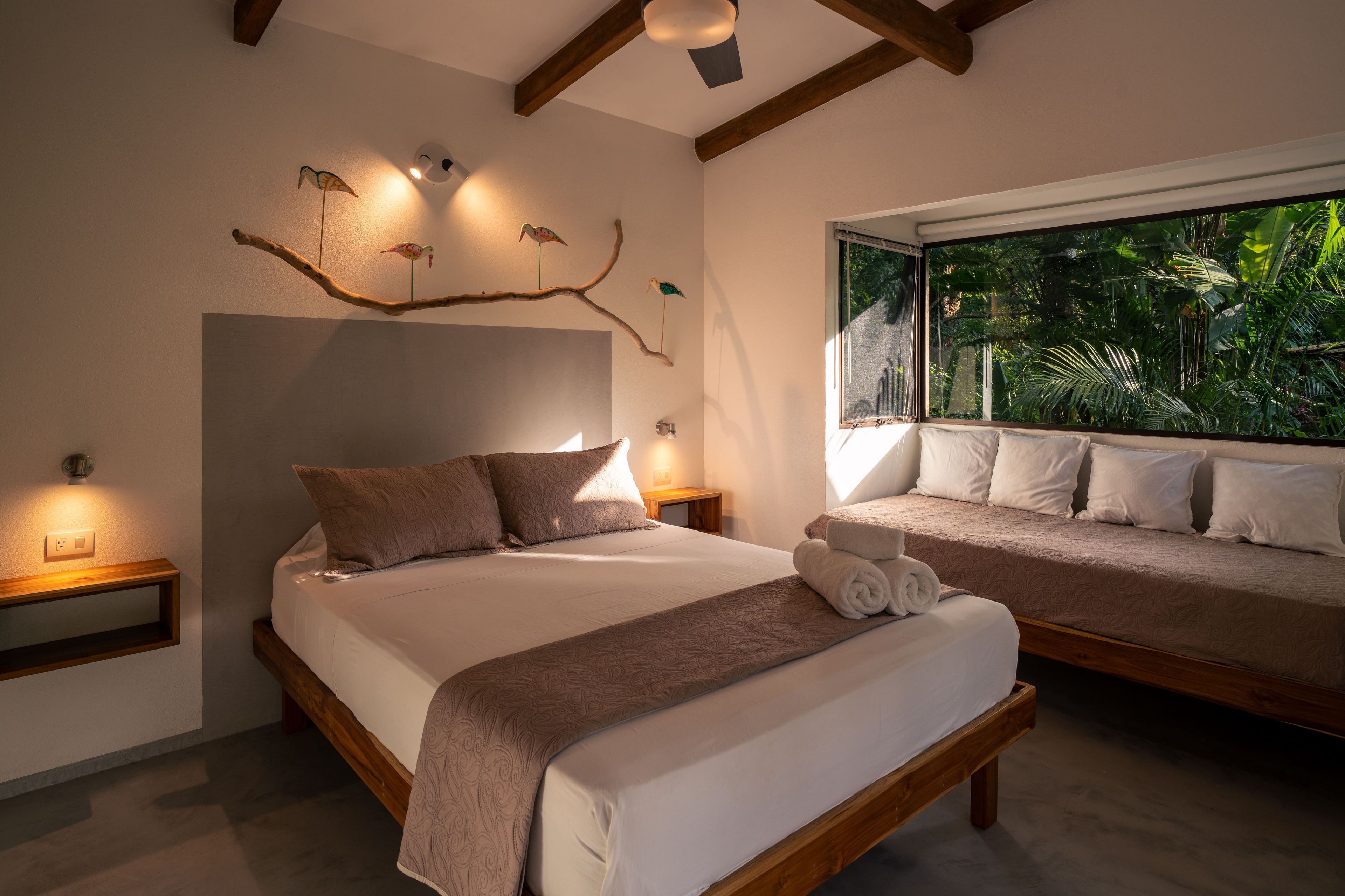 Un dormitorio con una cama grande, una cama más pequeña y una ventana con vistas a zonas verdes.