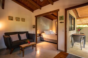 A cozy room with a sofa, a small table, and a bed. There is a wooden ceiling and a window with a view.