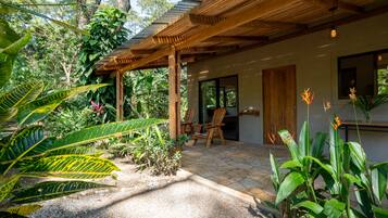 Een overdekt terras met een houten pergola, een stenen patio en weelderige tropische planten.