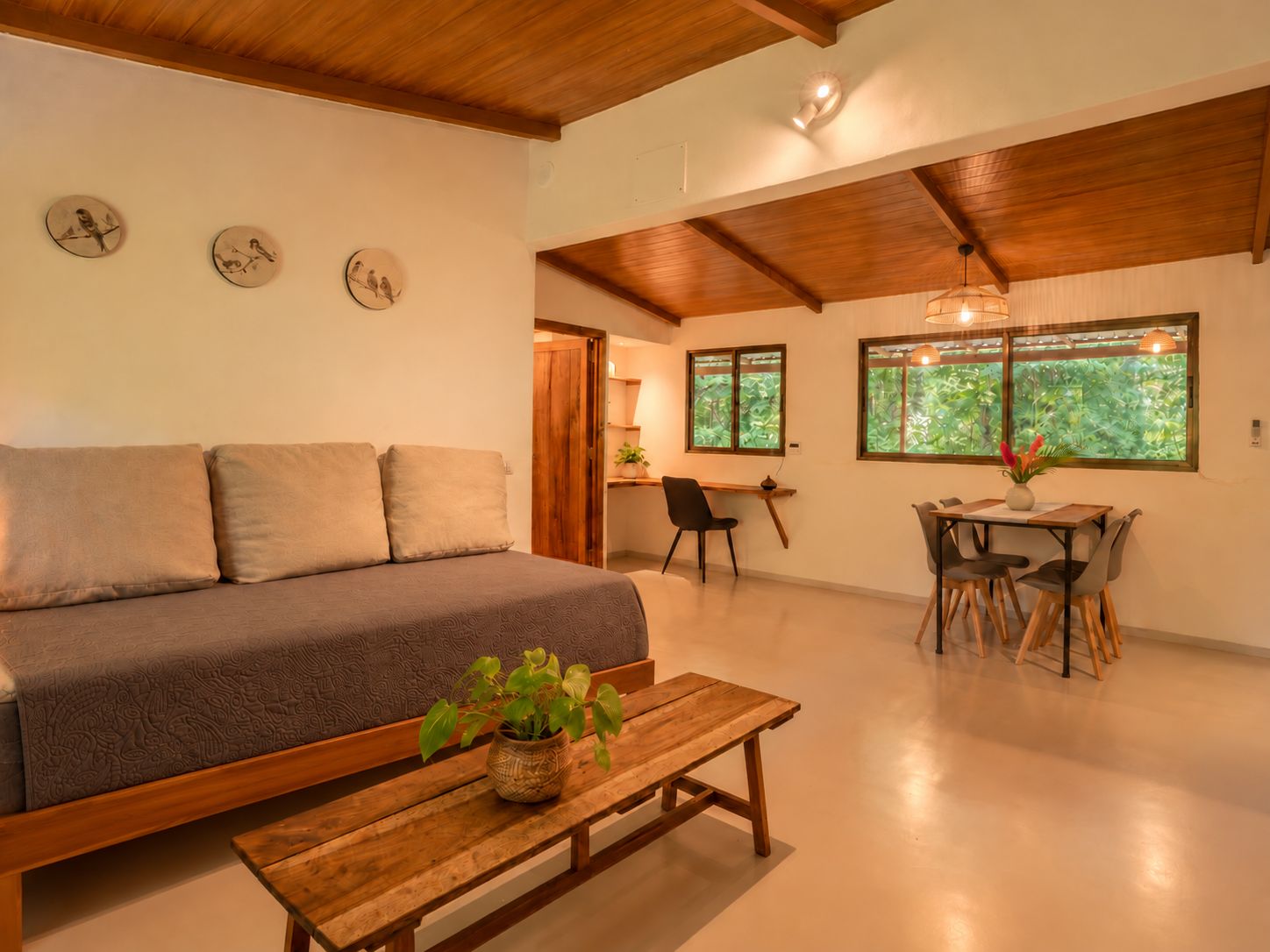 A spacious living area with a sofa, a dining table with chairs, and a wooden bench with a plant.