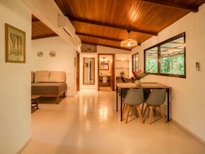 A modern interior with a wooden ceiling, a dining area with chairs and a table, a sofa, and a view through a window.