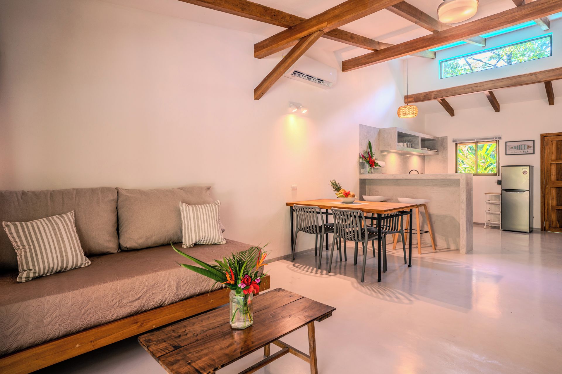 Una sala de estar moderna con un sofá, una mesa de comedor con sillas, una zona de cocina y un amplio ventanal.