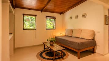 Una habitación acogedora con techo de madera, una cama, una mesita con una planta y dos ventanas con vistas a la vegetación.