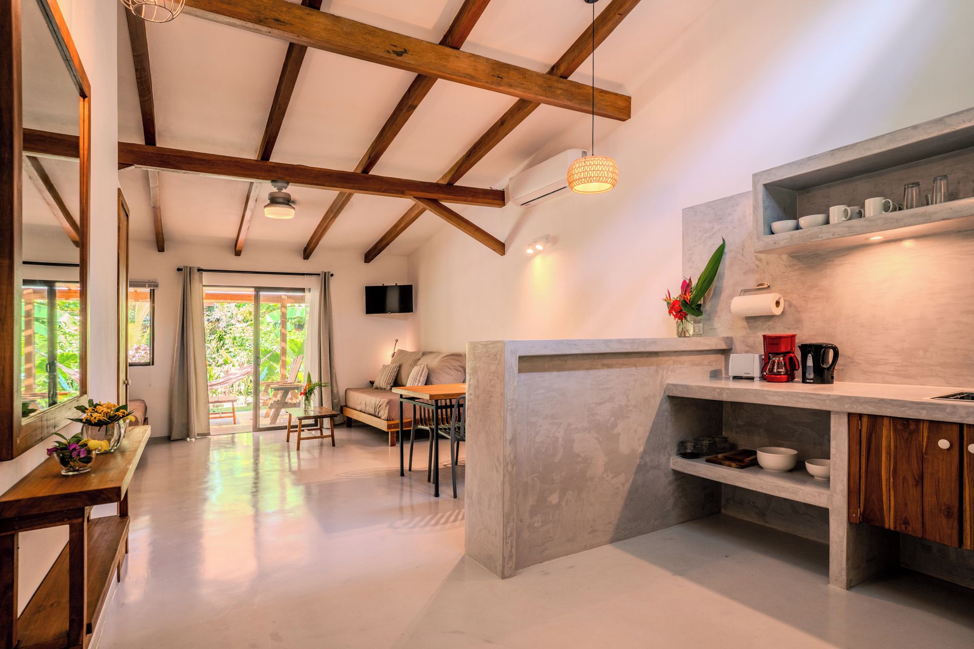 Una cocina moderna con una isla central, un comedor con sofá y sillas, y un ventanal con vistas a la vegetación.
