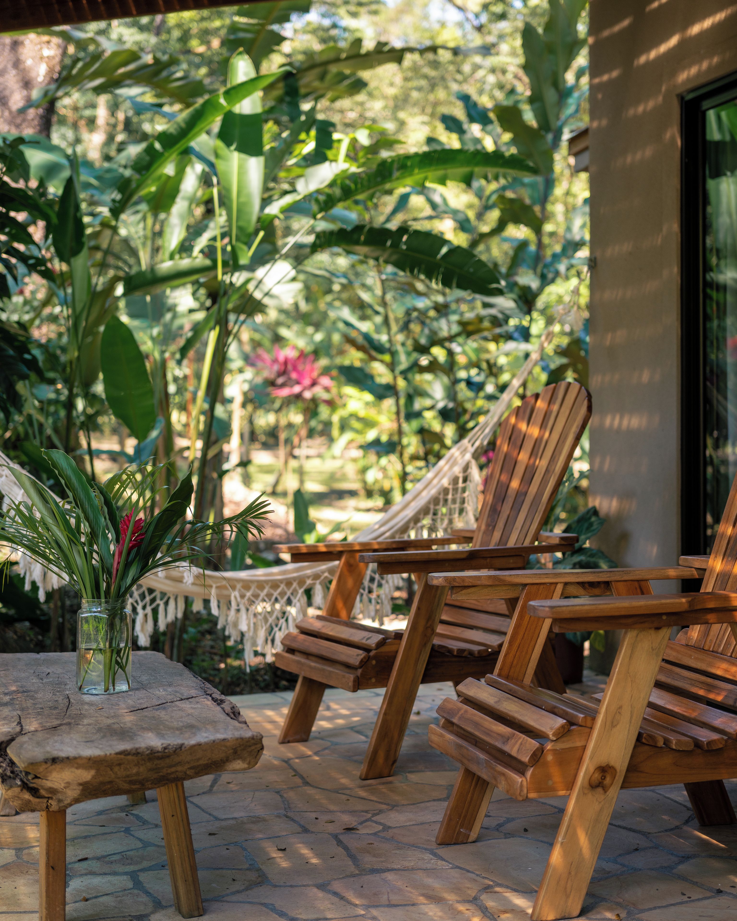 Terraza de madera con dos sillones de descanso y una mesita, rodeada de abundante vegetación y una hamaca.
