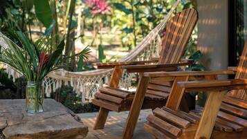 Terraza de madera con dos sillones de descanso y una mesita, rodeada de abundante vegetación y una hamaca.