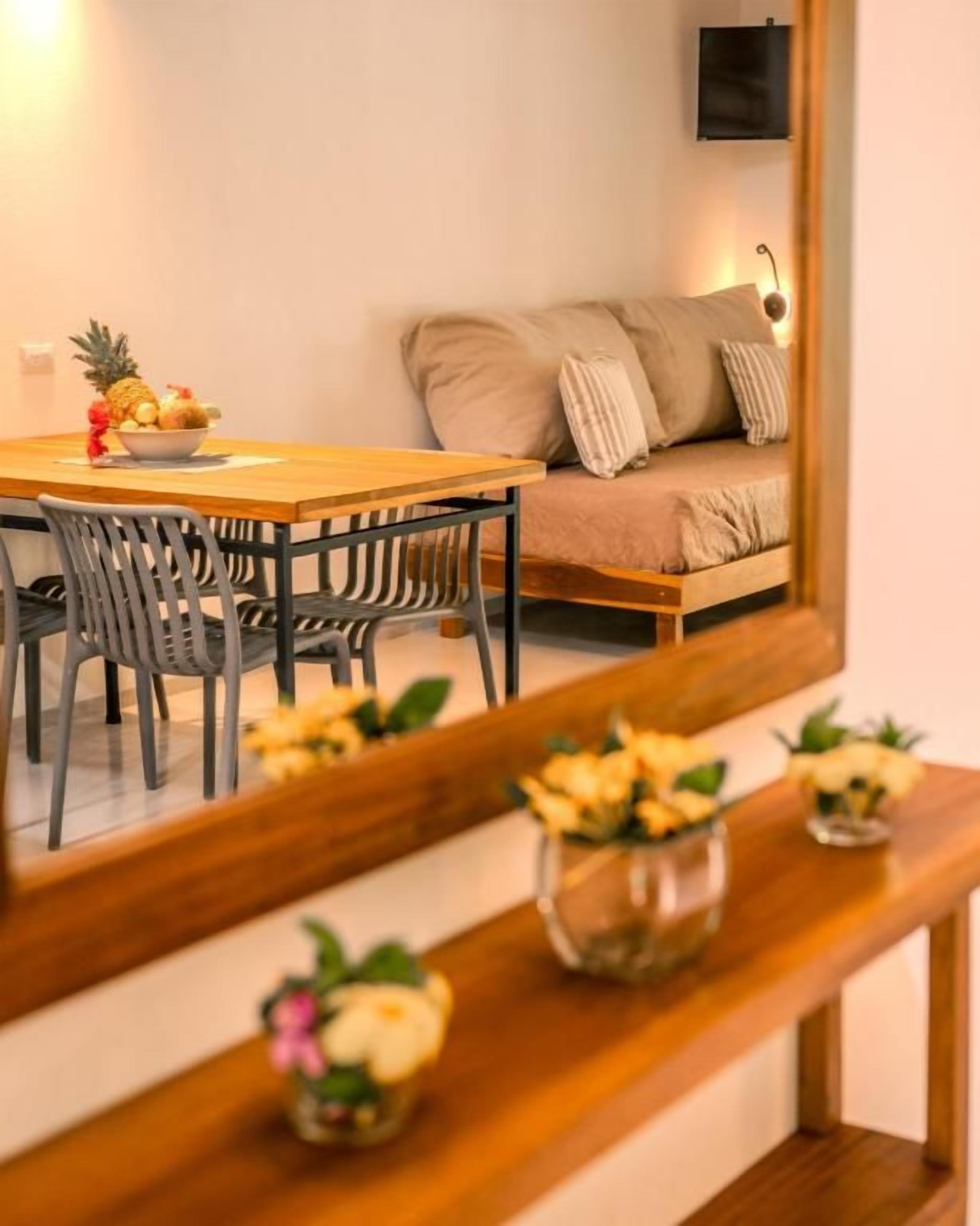 Un área de comedor con una mesa y sillas de madera, un sofá y un espejo que refleja la habitación.