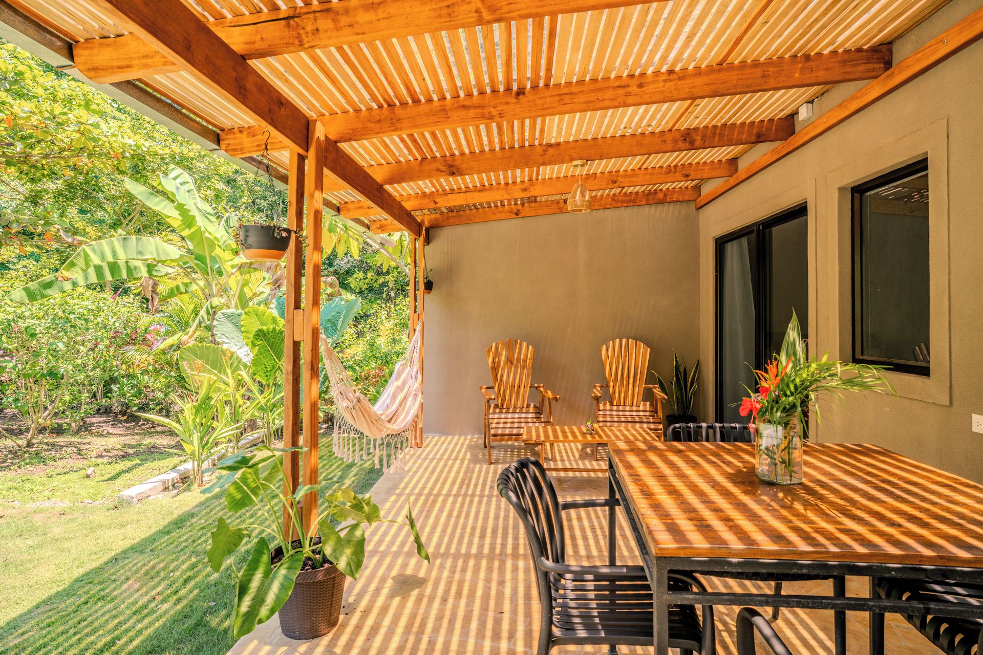 An outdoor patio with a wooden pergola, a hammock, and a table with chairs.