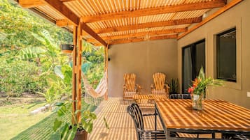 An outdoor patio with a wooden pergola, a hammock, and a table with chairs.