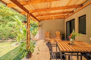 An outdoor patio with a wooden pergola, a hammock, and a table with chairs.