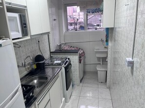 A compact kitchen with a microwave, stove, sink, and a window with a view of buildings. - Suitable for weekends and holidays, very close to the beach - Vila Guilhermina (Praia Grande)