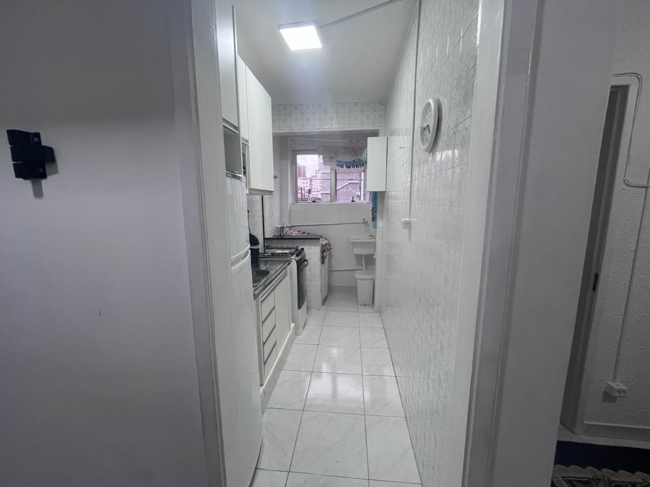 A narrow hallway with a kitchen area, including cabinets and a sink.