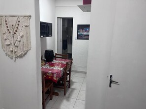 Uma pequena sala de jantar com mesa posta para dois, televisão na parede e uma porta que dá para outro espaço.