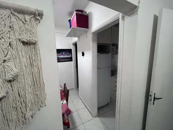 Corredor estreito com cozinha, geladeira e porta que dá para outro quarto.