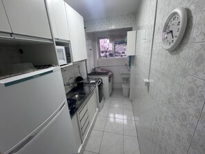 A compact kitchen with white cabinets, a microwave, a sink, and a clock on the wall. - Suitable for weekends and holidays, very close to the beach - Vila Guilhermina (Praia Grande)