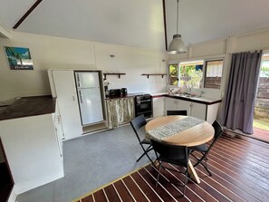 A compact kitchen with a refrigerator, stove, and microwave. There is a dining table with chairs, and a window with curtains.