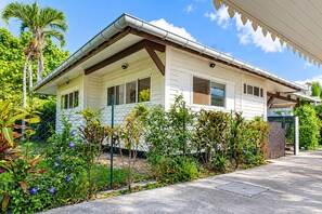 A single-story house with a porch, surrounded by a variety of plants and a clear sky.