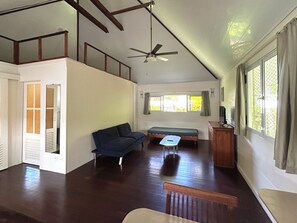 A spacious room with a high ceiling, a ceiling fan, a bed, a sofa, and a small table.