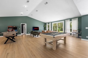 Ein großzügiges Wohnzimmer mit Billardtisch, Kicker, Fernseher und einer Couch.