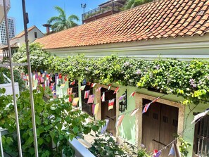 A building with a tiled roof and a balcony with plants. Flags are hanging on the balcony. - by Calamari.Homes - Centenario Casa 206 - Old City (Cartagena de Indias)