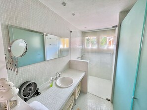 Une salle de bain avec un grand miroir, un lavabo, un ventilateur et un espace douche.