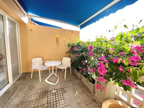 Un espace extérieur abrité, aménagé avec une table et des chaises, et entouré de plantes en pot et d’arbustes à fleurs.