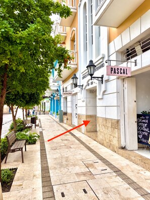 A street with a row of buildings, a tree-lined sidewalk, and a red arrow pointing to a building with a sign that reads 'PASCAL.' - by Calamari.Homes - Centenario Casa 206 - Old City (Cartagena de Indias)