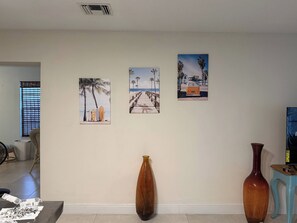 Quarto com uma grande janela, uma mesa de madeira com papéis, um vaso marrom e dois vasos no chão.