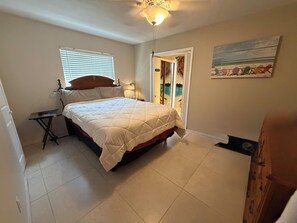 Quarto com cama, mesa de cabeceira, janela com persianas, porta para uma varanda e um quadro na parede.