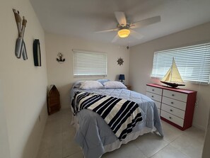 Ein Schlafzimmer mit einem Bett, einem Deckenventilator, einer Kommode und einer Segelboot-Dekoration.