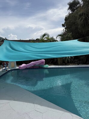 Ein Swimmingpool mit blauer Plane, umgeben von Palmen und blauem Himmel.