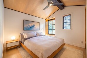 Ein Schlafzimmer mit einem Bett, einem Nachttisch, einem Deckenventilator, einem Fenster und einem Gemälde an der Wand.